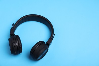 Photo of Pair of stylish black headphones on light blue background, above view. Space for text