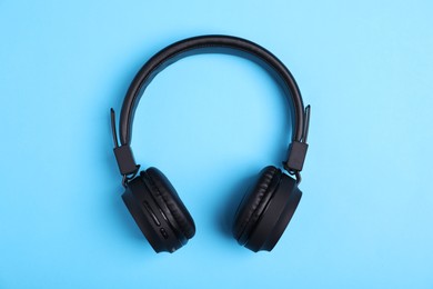 Photo of Pair of stylish black headphones on light blue background, top view