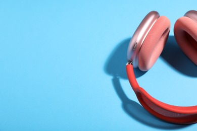 Photo of Pair of stylish pink headphones on light blue background, above view. Space for text