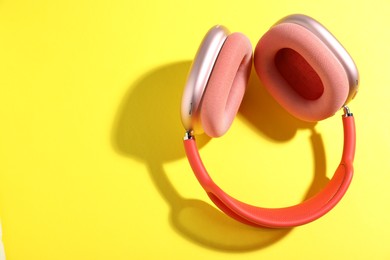Photo of Pair of stylish pink headphones on yellow background, top view. Space for text