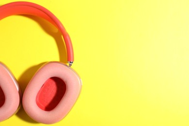 Photo of Pair of stylish pink headphones on yellow background, top view. Space for text