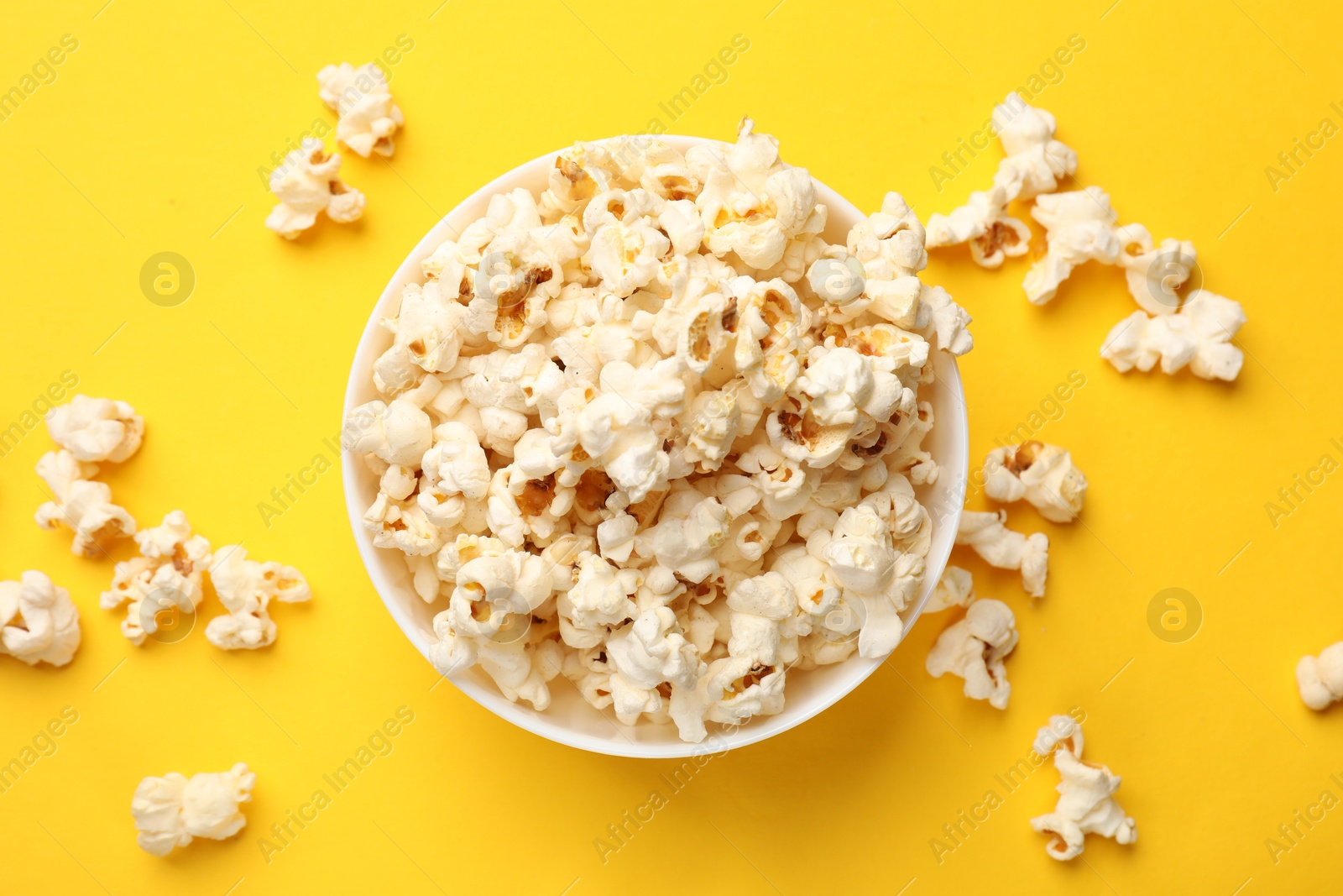 Photo of Tasty popcorn in bowl on yellow background, flat lay