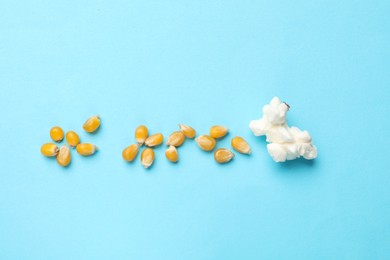 Photo of Tasty popcorn and dry kernels on light blue background, flat lay
