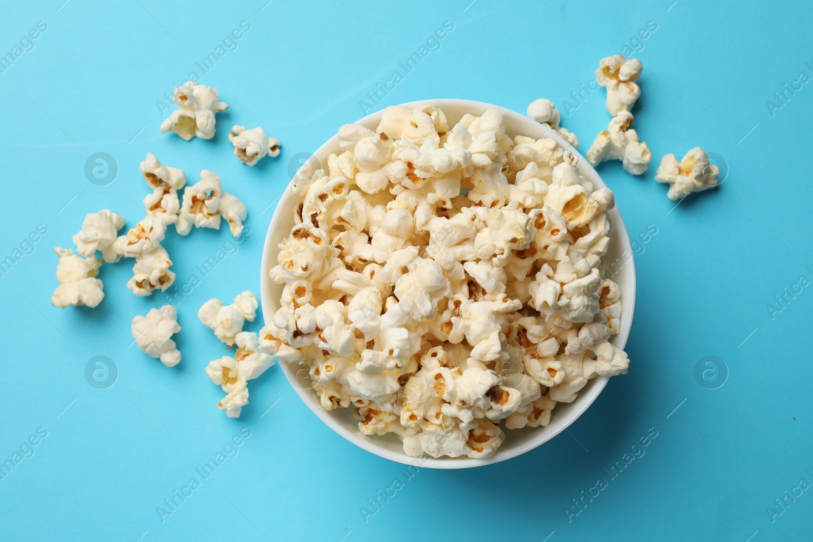 Tasty popcorn in bowl on light blue background, flat lay Photo of Tasty popcorn in bowl on light blue background, flat lay