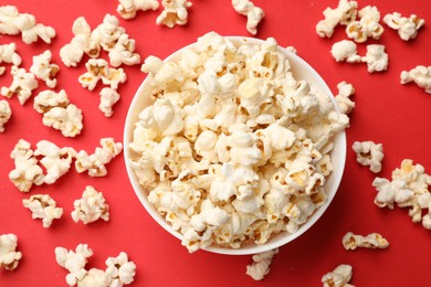 Photo of Tasty popcorn in bowl on red background, flat lay