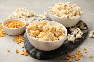 Photo of Tasty popcorn and corn kernels on light grey table, closeup