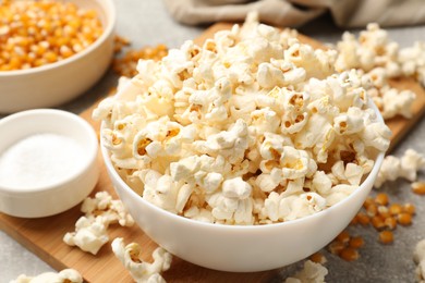 Photo of Tasty popcorn and corn kernels on light grey table, closeup
