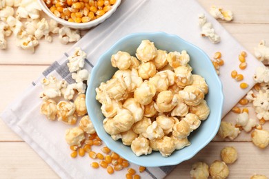 Photo of Tasty popcorn and corn kernels on light wooden table, flat lay