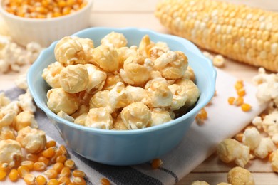 Photo of Tasty popcorn and corn kernels on light wooden table, closeup