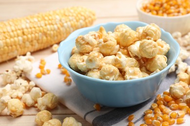Photo of Tasty popcorn and corn kernels on light wooden table, closeup