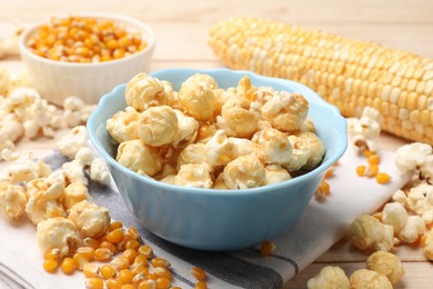Photo of Tasty popcorn and corn kernels on light wooden table, closeup