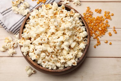 Photo of Tasty popcorn and corn kernels on light wooden table, flat lay