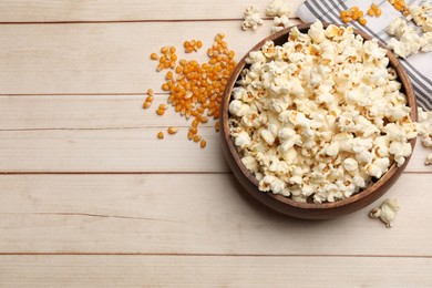 Photo of Tasty popcorn and corn kernels on light wooden table, flat lay. Space for text