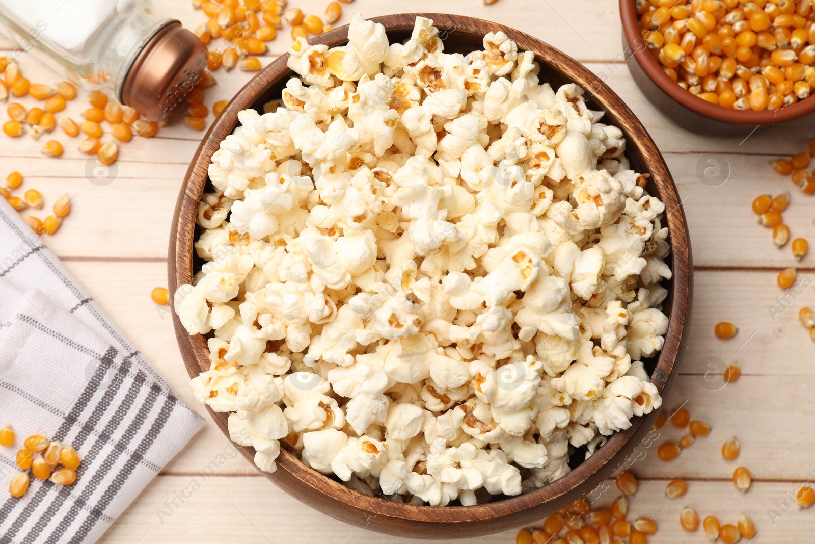 Photo of Tasty popcorn and corn kernels on light wooden table, flat lay