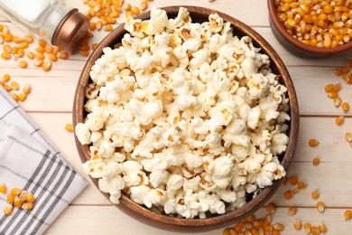 Photo of Tasty popcorn and corn kernels on light wooden table, flat lay