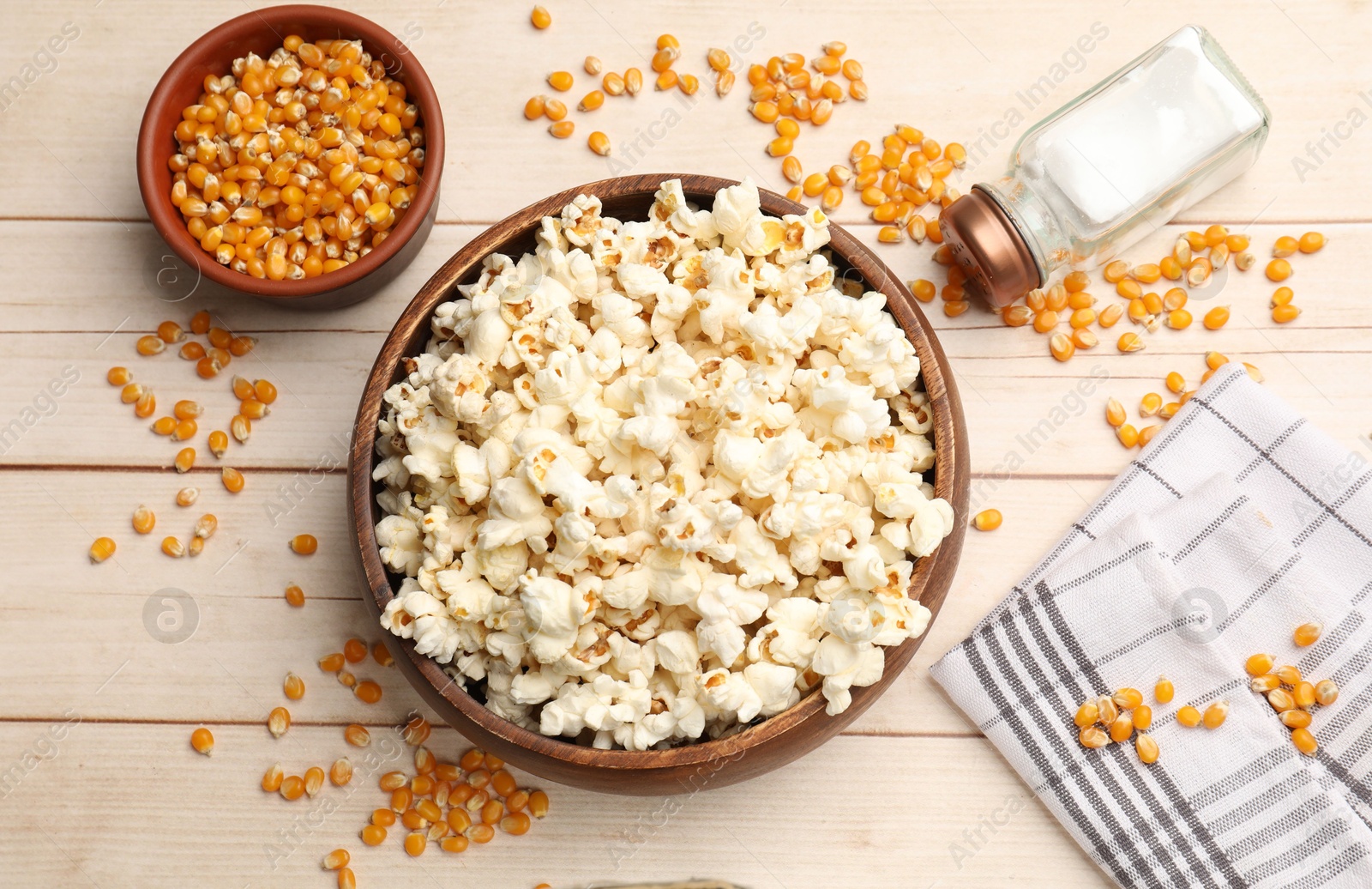 Photo of Tasty popcorn and corn kernels on light wooden table, flat lay