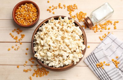 Photo of Tasty popcorn and corn kernels on light wooden table, flat lay