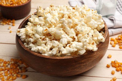 Photo of Tasty popcorn and corn kernels on light wooden table, closeup