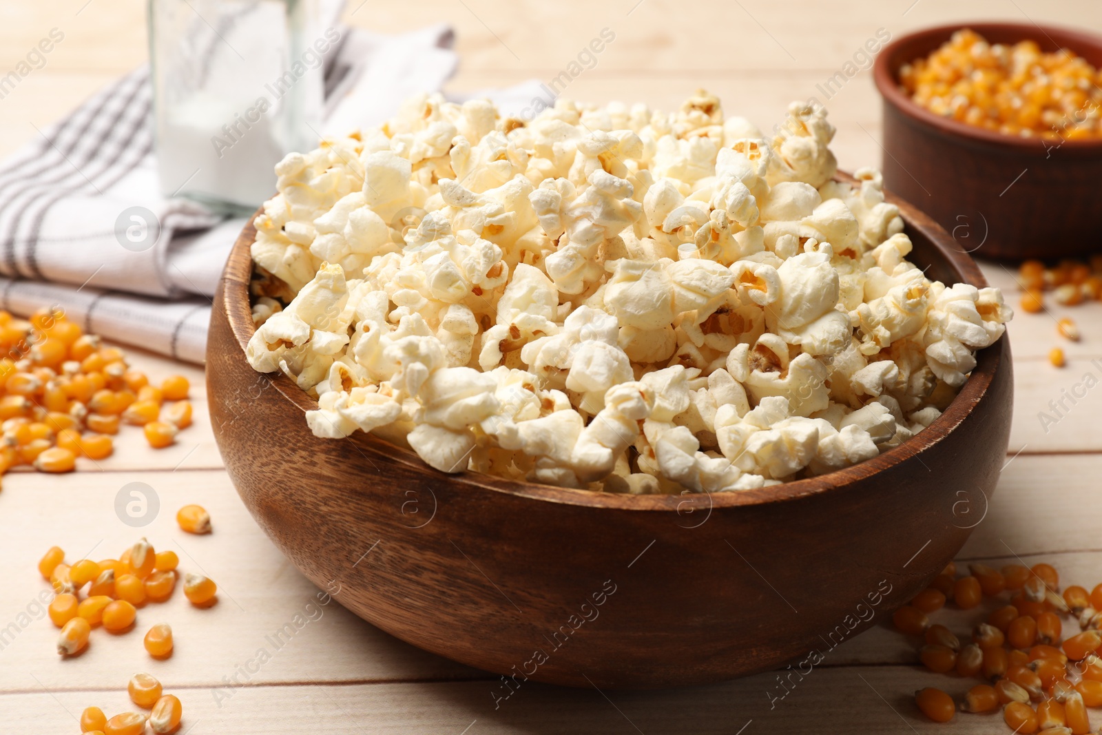 Photo of Tasty popcorn and corn kernels on light wooden table, closeup