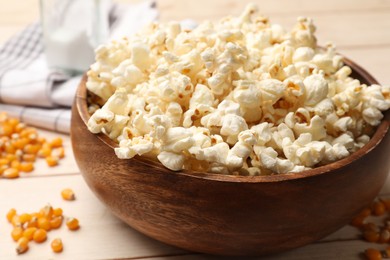 Photo of Tasty popcorn and corn kernels on light wooden table, closeup