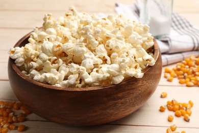 Photo of Tasty popcorn and corn kernels on light wooden table, closeup