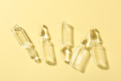 Photo of Glass ampoules with liquid on yellow background, flat lay