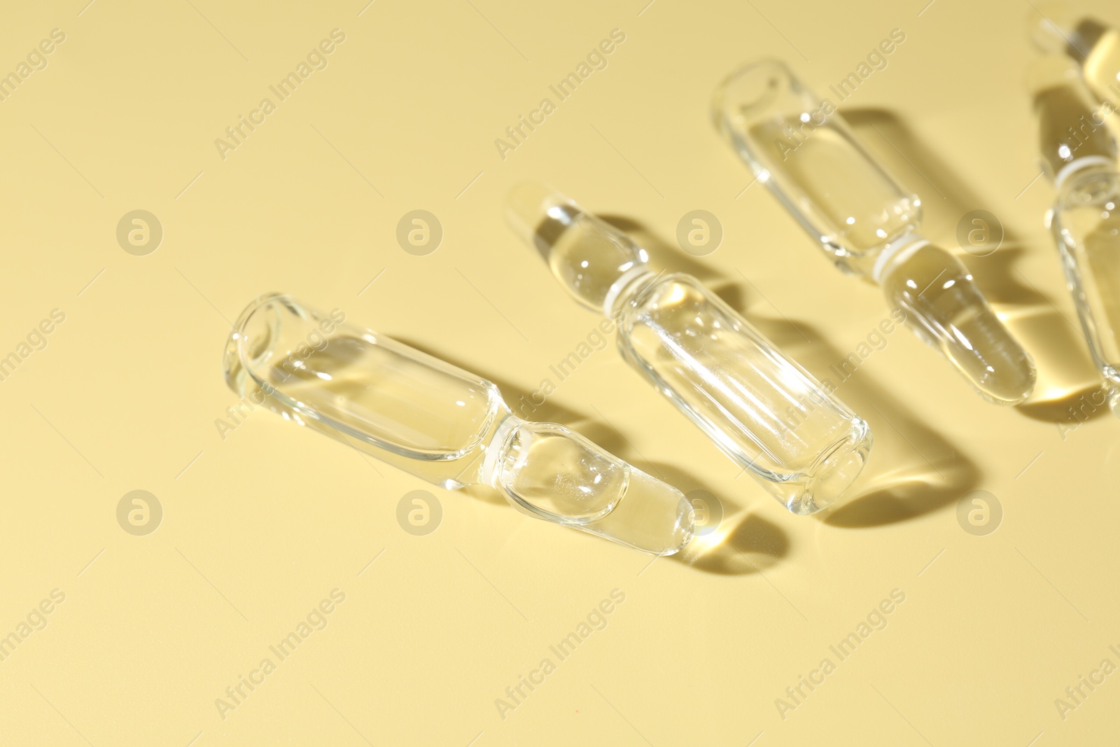 Photo of Glass ampoules with liquid on yellow background, flat lay