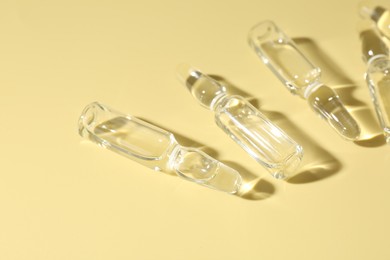 Photo of Glass ampoules with liquid on yellow background, flat lay