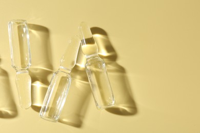 Photo of Glass ampoules with liquid on yellow background, flat lay