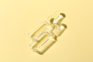 Photo of Glass ampoules with liquid on yellow background, flat lay