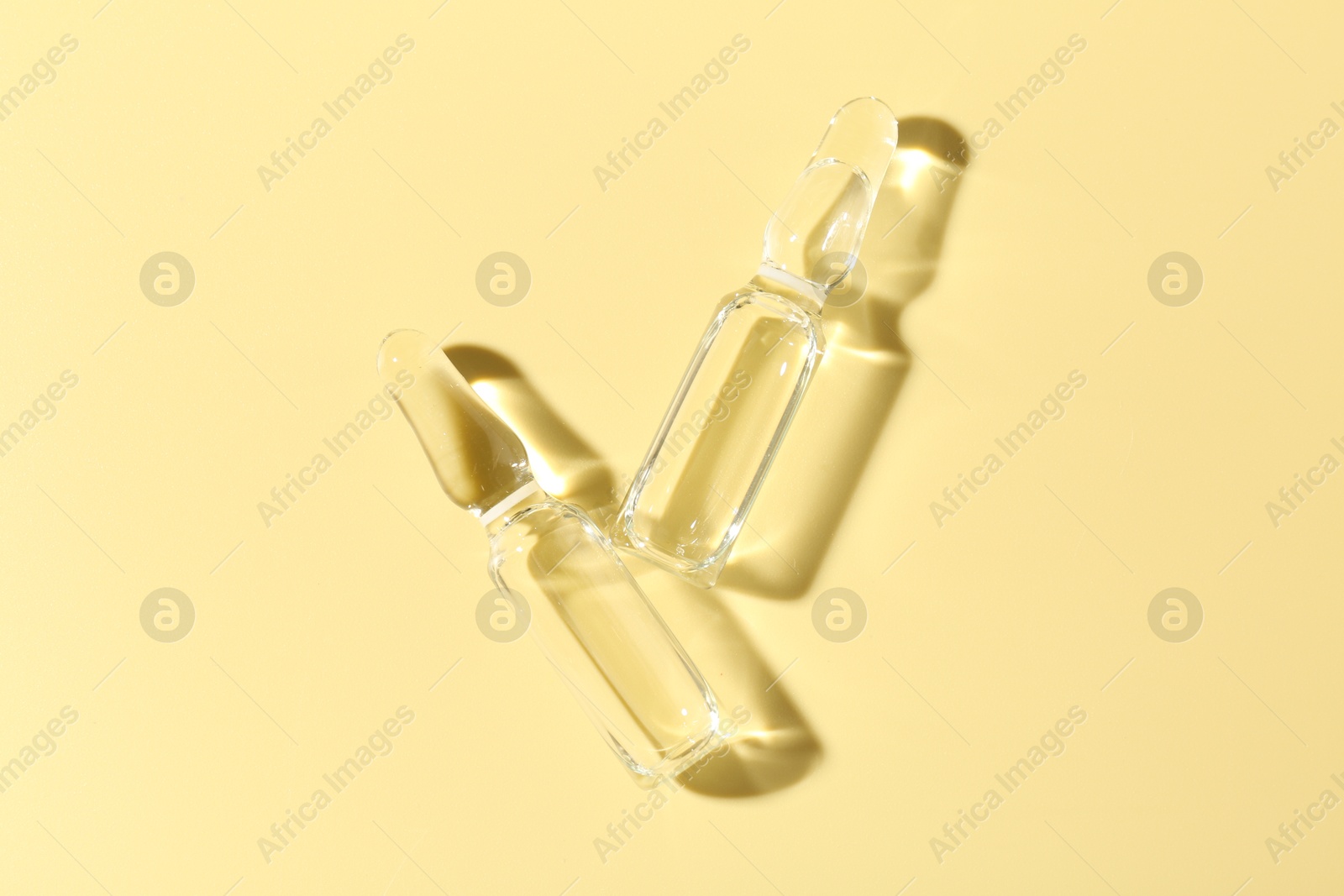 Glass ampoules with liquid on yellow background, flat lay Photo of Glass ampoules with liquid on yellow background, flat lay