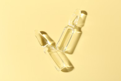 Photo of Glass ampoules with liquid on yellow background, flat lay