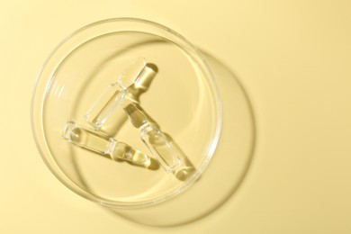 Photo of Glass ampoules with liquid and Petri dish on yellow background, top view. Space for text