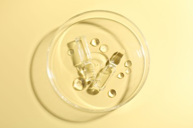 Photo of Glass ampoules with liquid and Petri dish on yellow background, top view