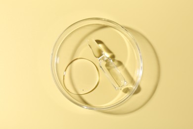 Photo of Glass ampoule with liquid and Petri dish on yellow background, top view