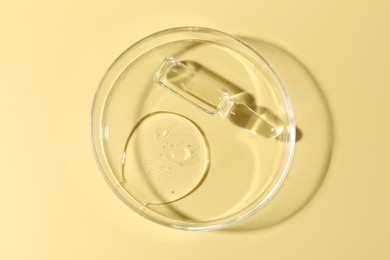Photo of Glass ampoule with liquid and Petri dish on yellow background, top view