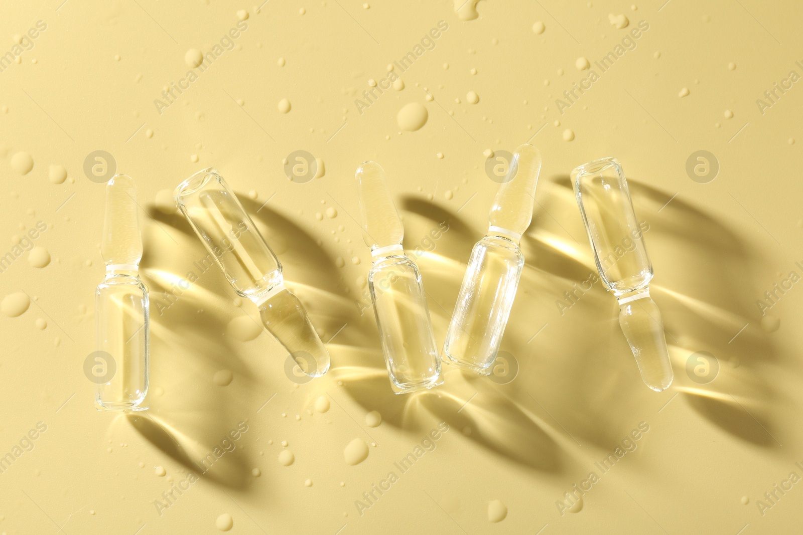 Glass ampoules with liquid and water drops on yellow background, flat lay Photo of Glass ampoules with liquid and water drops on yellow background, flat lay
