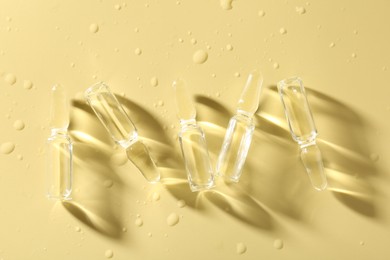 Photo of Glass ampoules with liquid and water drops on yellow background, flat lay