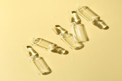 Photo of Glass ampoules with liquid on yellow background, flat lay
