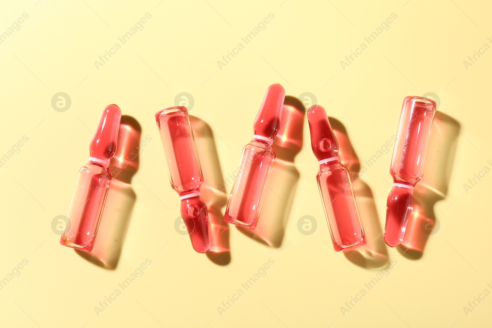 Glass ampoules with liquid on yellow background, flat lay Photo of Glass ampoules with liquid on yellow background, flat lay