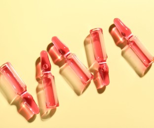 Photo of Glass ampoules with liquid on yellow background, flat lay