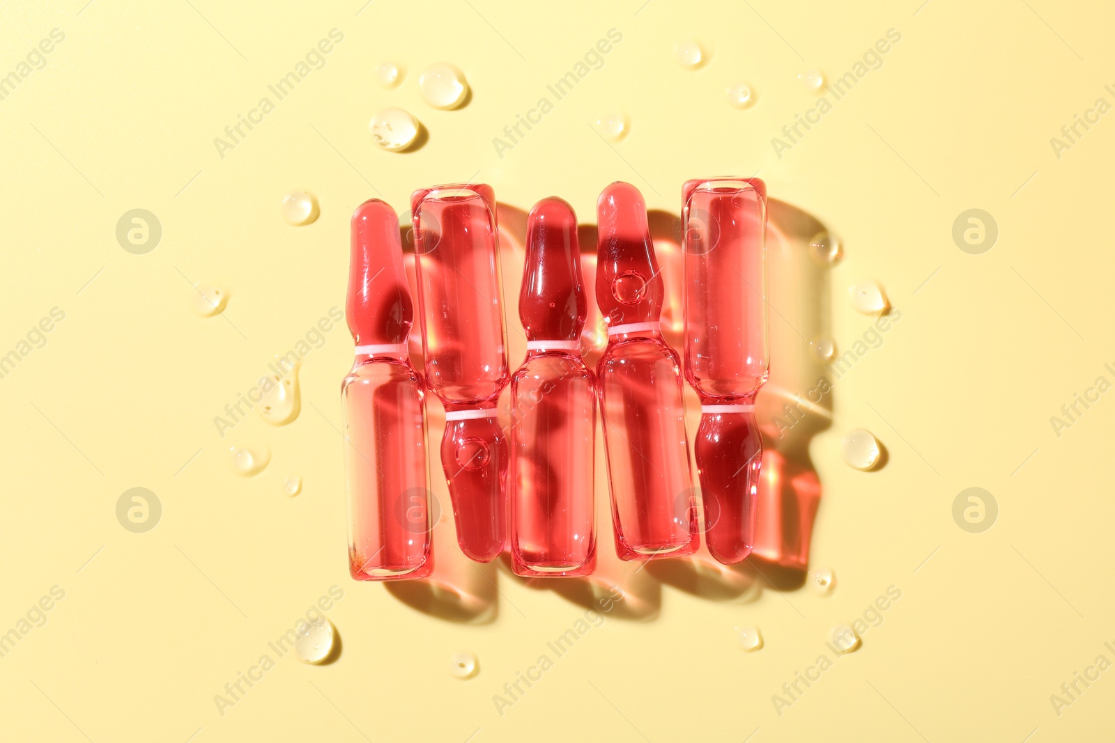 Glass ampoules with liquid and water drops on yellow background, flat lay Photo of Glass ampoules with liquid and water drops on yellow background, flat lay