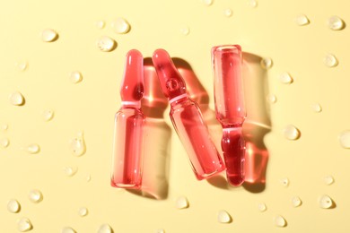 Photo of Glass ampoules with liquid and water drops on yellow background, flat lay