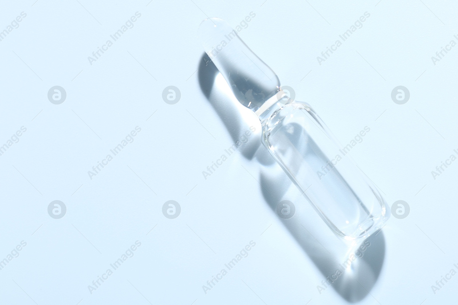 Glass ampoule with liquid on light blue background, top view. Space for text Photo of Glass ampoule with liquid on light blue background, top view. Space for text