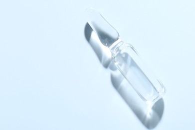 Photo of Glass ampoule with liquid on light blue background, top view. Space for text