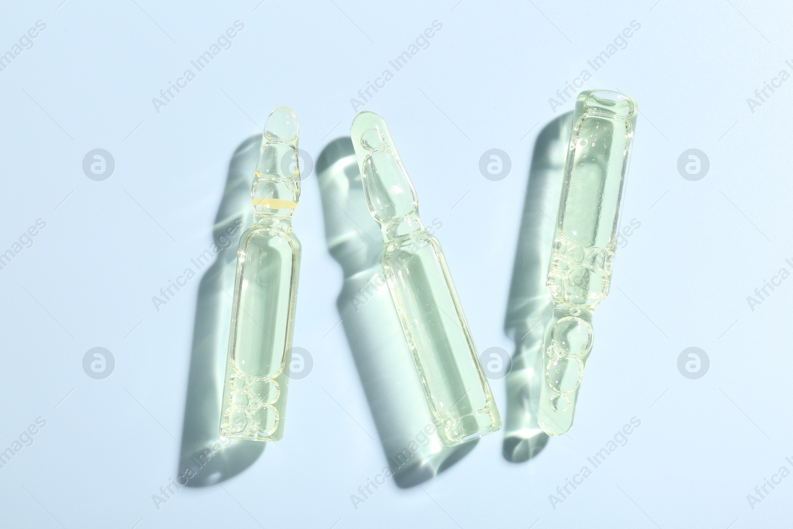 Glass ampoules with liquid on light blue background, flat lay Photo of Glass ampoules with liquid on light blue background, flat lay