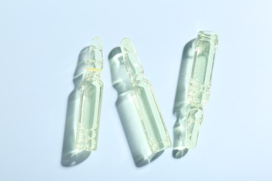 Photo of Glass ampoules with liquid on light blue background, flat lay