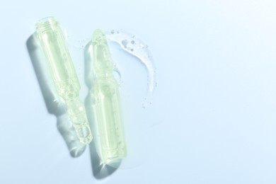 Photo of Glass ampoules with liquid on light blue background, flat lay