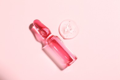 Photo of Glass ampoule with liquid on pink background, top view