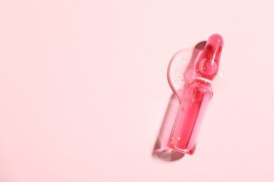 Photo of Glass ampoule with liquid on pink background, top view. Space for text